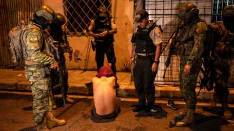 Soldados vigilan a un hombre detenido en Guayaquil durante una patrulla de toque de queda