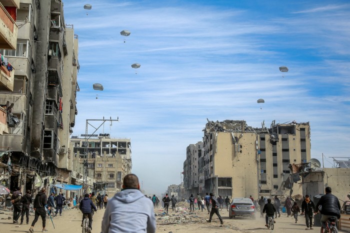 Palestinos corren por una calle mientras se lanza ayuda humanitaria desde el aire en la ciudad de Gaza 