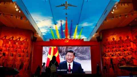 Los visitantes se paran frente a una pantalla gigante que muestra a Xi Jinping, en el Museo Militar de la Revolución Popular China en Beijing.  En el techo se proyecta una imagen de un avión con estelas de humo multicolores.