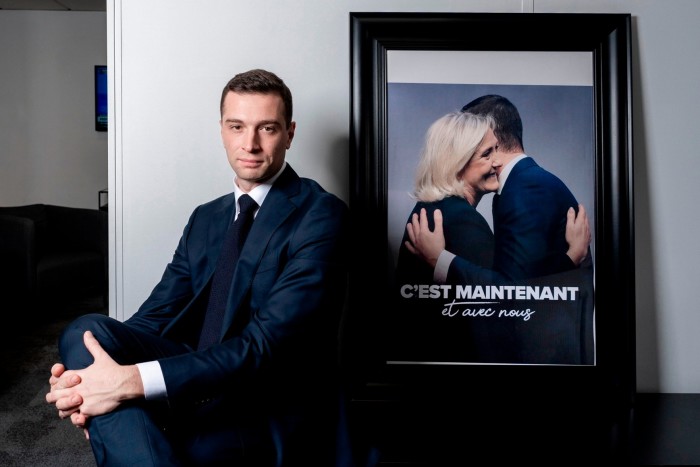 Jordan Bardella frente a una fotografía que lo muestra a él y a Marine Le Pen abrazados