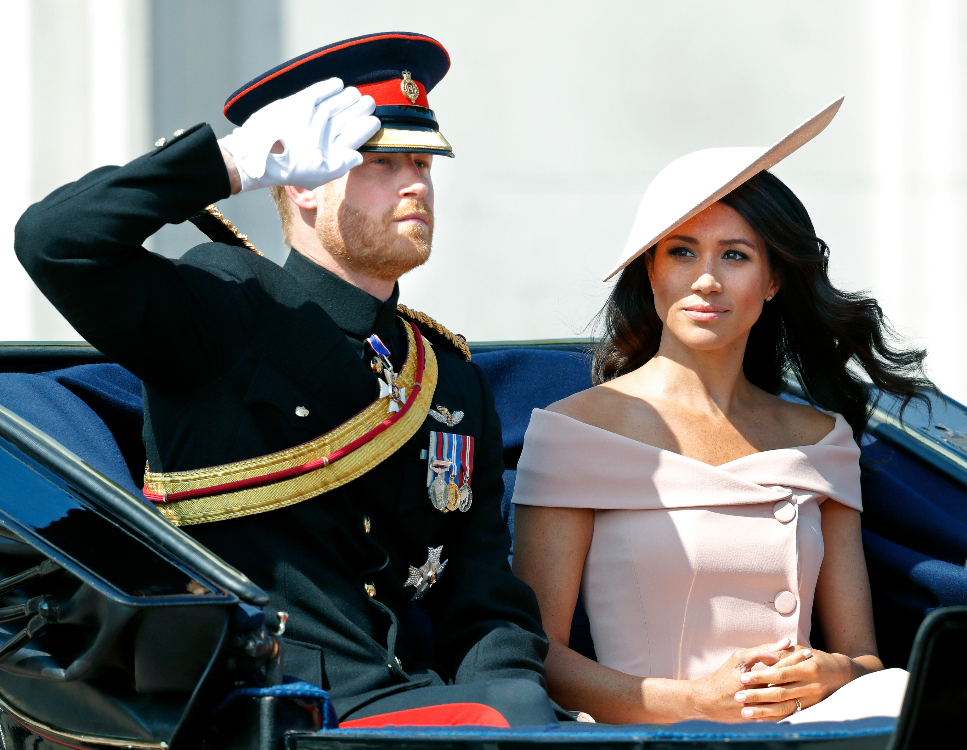 El duque en 2018 vistiendo prendas militares y saludando a la multitud mientras su esposa Meg se sienta a su lado.