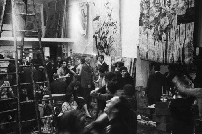 La gente se mezcla en una fiesta en el estudio de un artista tipo loft con pinturas en las paredes.