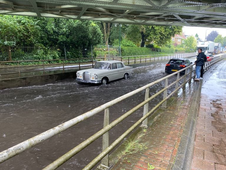 Coche varado bajo un viaducto lleno de agua. 