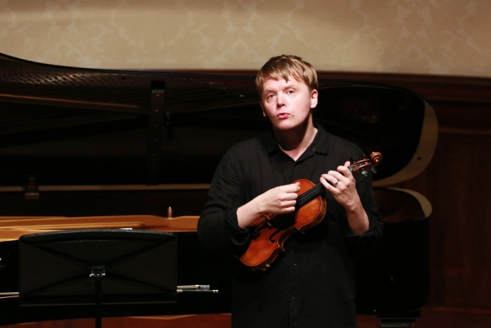 Un hombre rubio se sienta con un violín en la mano.
