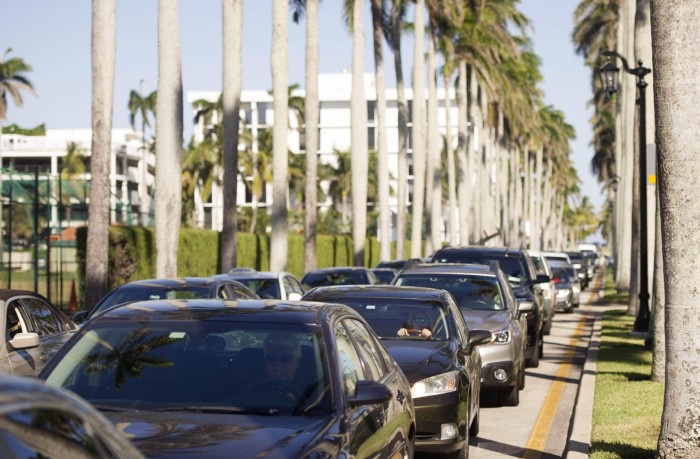 Una fila de autos atrapados en el tráfico en un día soleado, con altas palmeras bordeando la carretera