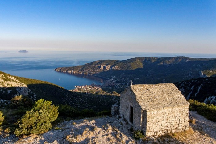 Una pequeña capilla de piedra en la cima de una colina con vistas a la bahía y al mar.