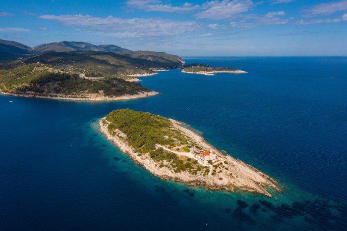 Vista aérea de un edificio al final de una isla en el mar azul, con una costa detrás.
