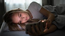 La chica se encuentra en la cama con el teléfono inteligente