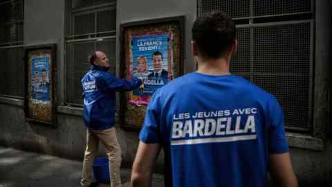 Dos hombres pegan carteles políticos franceses en edificios