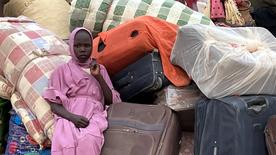 Una joven sudanesa sentada entre maletas en un campo de refugiados