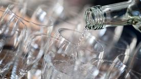 Varios vasos se encuentran uno al lado del otro en una tableta.  Se vierte agua en un vaso desde una botella de vidrio.