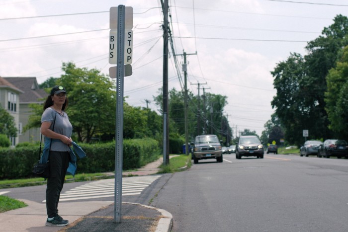 Una mujer con gorra se encuentra en la esquina de una calle en los suburbios de los Estados Unidos. 