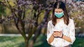 Una mujer con una máscara se encuentra en el parque y mira el teléfono inteligente