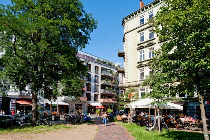 Una calle de la ciudad con bloques de apartamentos de 5 a 6 plantas y cafeterías a nivel de la calle.