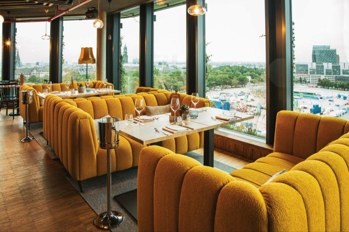 Un salón de hotel con modernos sofás naranjas junto a ventanas panorámicas.