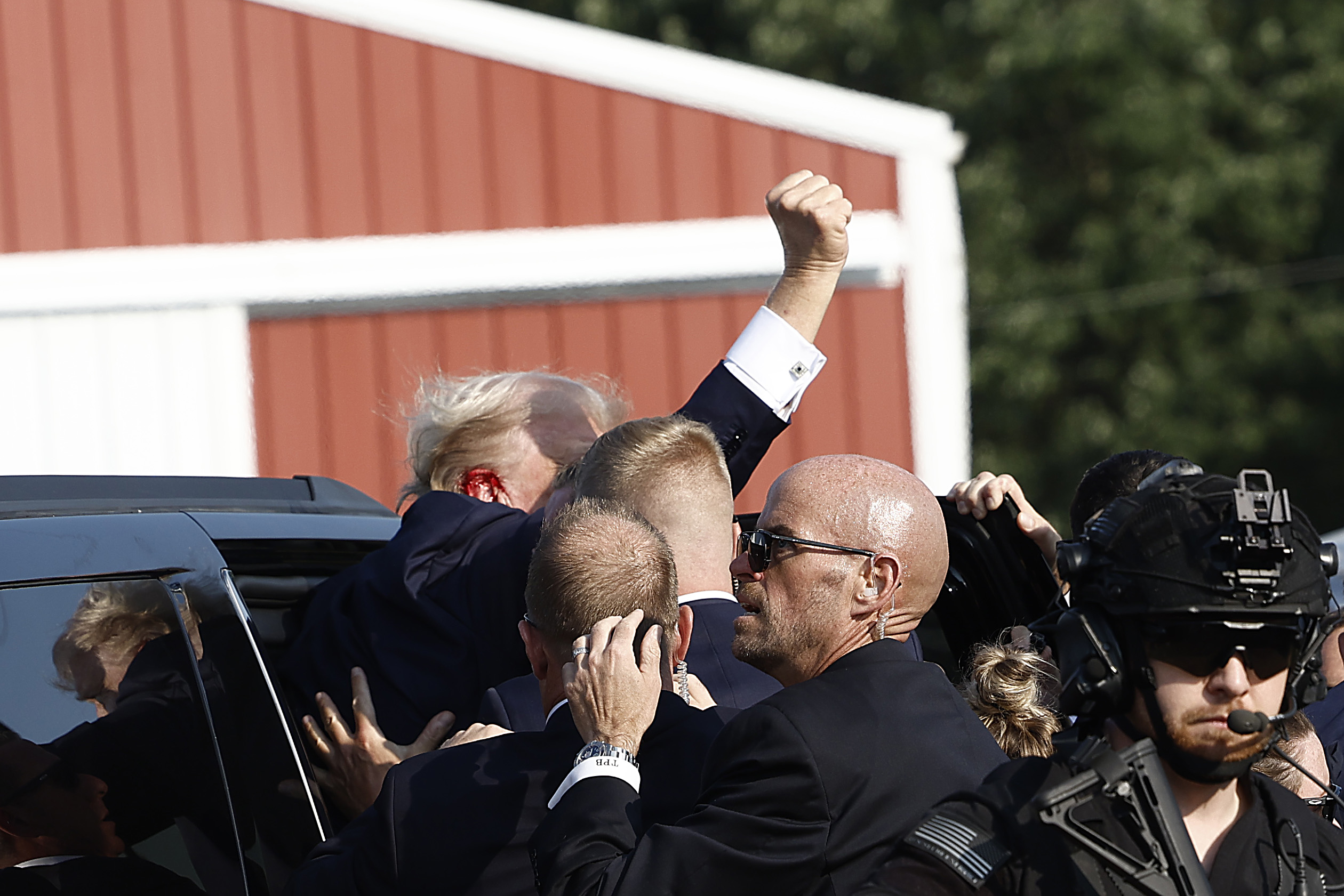 Trump golpea el aire con el puño mientras lo meten en un auto y se lo llevan.