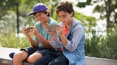 Juegos para móviles: dos niños se sientan uno al lado del otro con sus smartphones