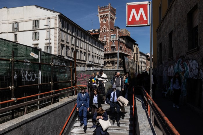 La gente baja las escaleras hacia la estación de metro M2 Sant'Ambrogio.