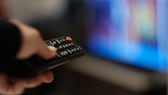 Imagen simbólica: una persona sostiene el control remoto frente a una pantalla de televisión borrosa