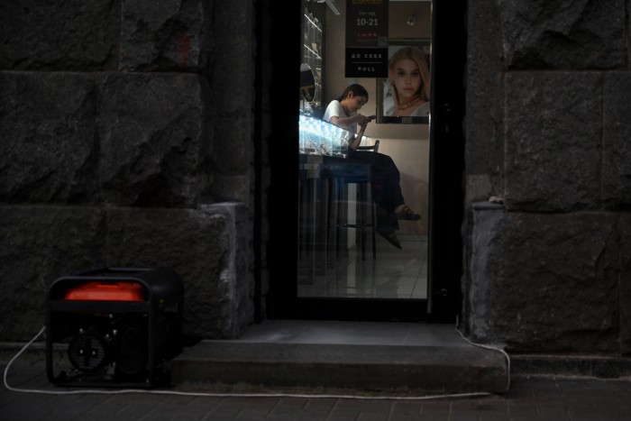 Una empleada de una joyería mira su teléfono inteligente mientras afuera funciona un generador eléctrico
