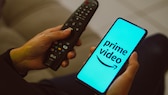 Logotipo de publicidad en video de Amazon Prime del servicio en un teléfono inteligente junto al control remoto para TV