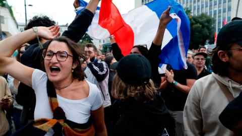 La gente ondea banderas francesas mientras reacciona a los resultados proyectados después de la segunda vuelta de las elecciones legislativas, el domingo.