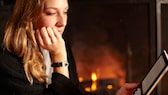 Mujer joven leyendo con un libro electrónico junto a la chimenea.  Surge la pregunta de cuáles son los mejores lectores de libros electrónicos en comparación.