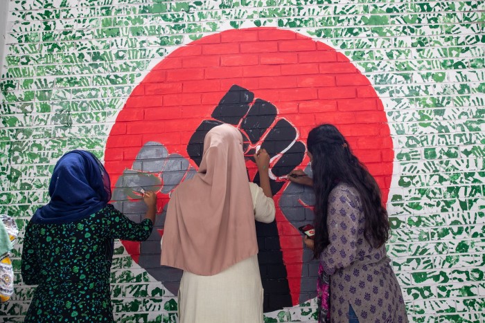 Tres mujeres pintan un cuadro de puños levantados en una pared.