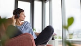 Imagen simbólica: Mujer escuchando música con auriculares supraaurales y mirando por la ventana