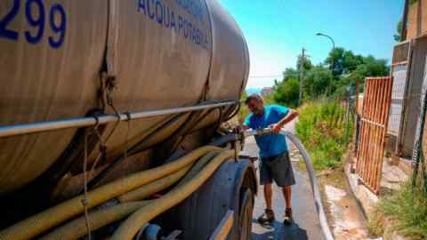 Un trabajador rellena un camión cisterna de agua.