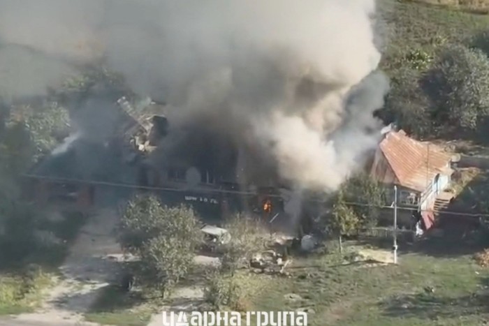 Salen columnas de humo de un edificio en llamas. El área circundante parece ser rural con algo de vegetación.