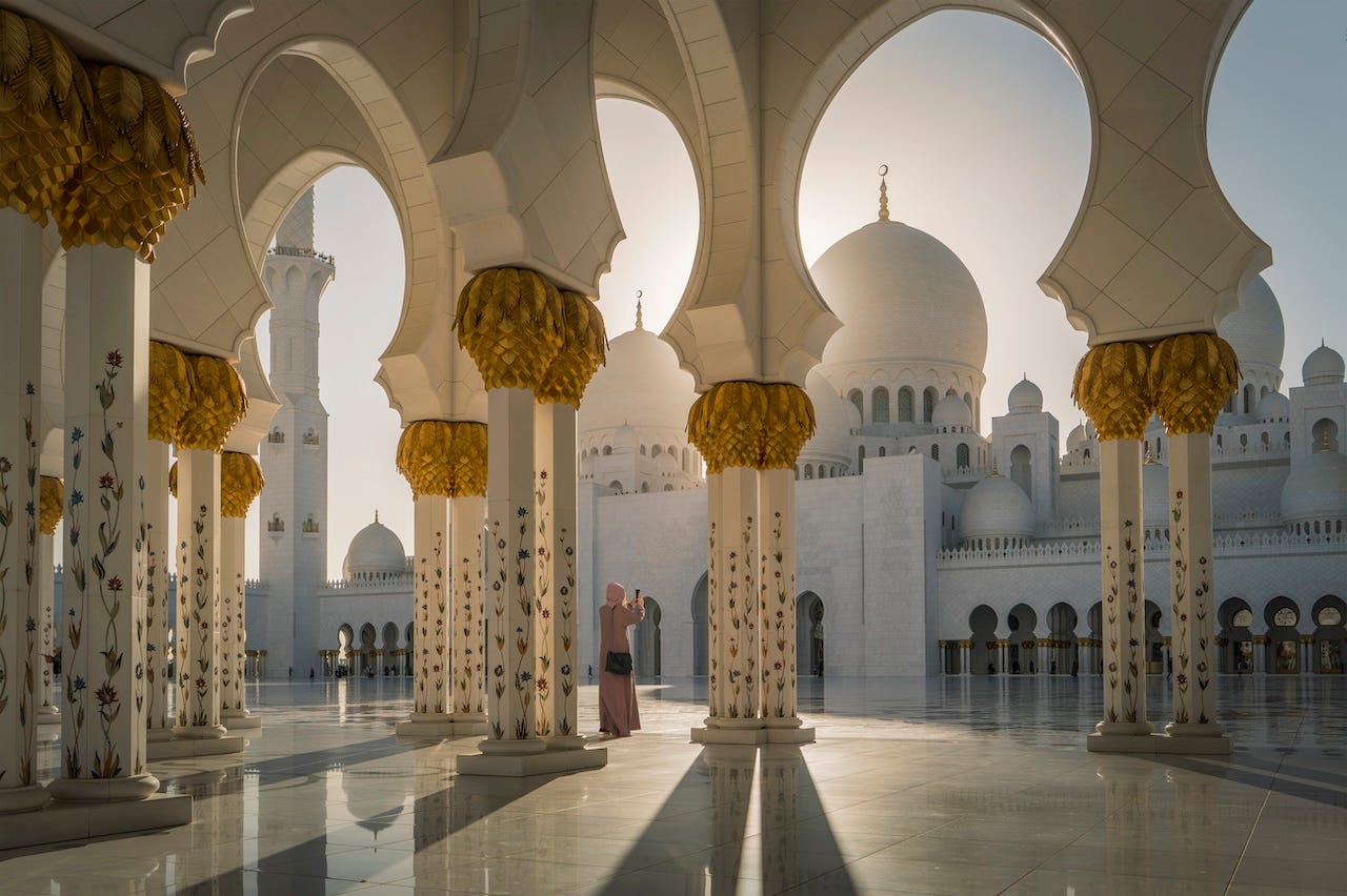 Una mujer tomando una fotografía mientras se encuentra entre los pilares blancos y dorados de la Gran Mezquita Sheik Zayed en Abu Dhabi.