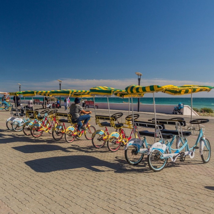 Bajo un cielo azul profundo, una fila de bicicletas de alquiler con toldos de rayas estacionadas en el paseo marítimo. 