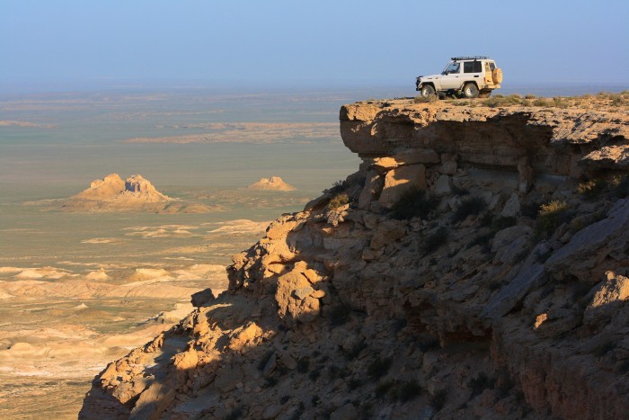 Un jeep posado en lo alto de un afloramiento rocoso con vistas al desierto.