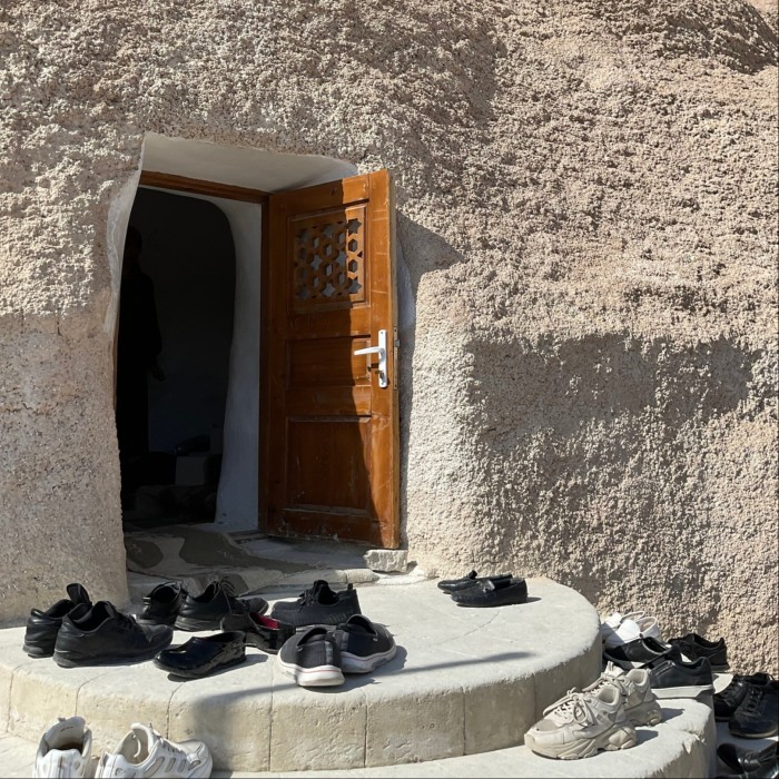 Una pequeña puerta de entrada a un santuario construido en la ladera de una roca. En los escalones que hay fuera de la puerta se han dejado varios pares de zapatos.