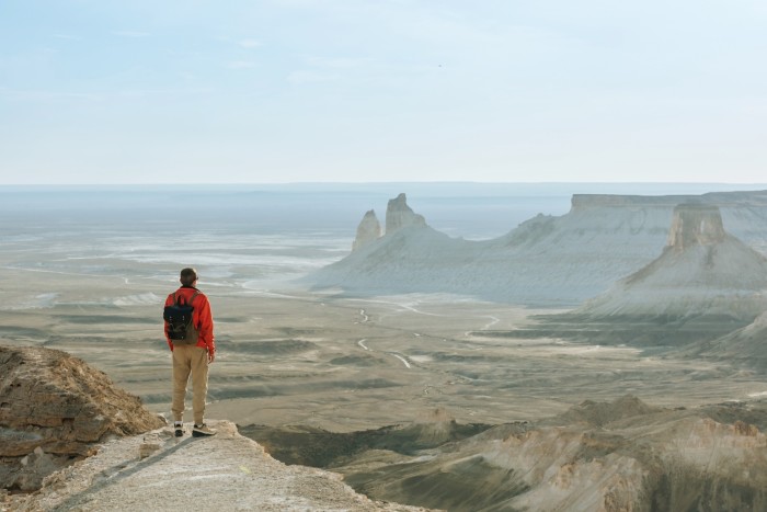 Un joven turista con una mochila en la cima de una montaña contemplando una vista de montañas y desierto.