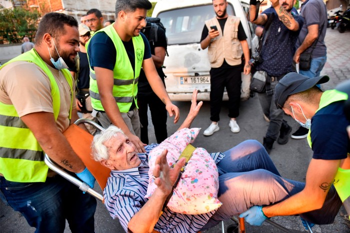 Los voluntarios llevan a un anciano en una silla mientras las personas que huyeron de sus aldeas en el sur del Líbano son recibidas en un instituto de arte transformado en un refugio para desplazados en Beirut.