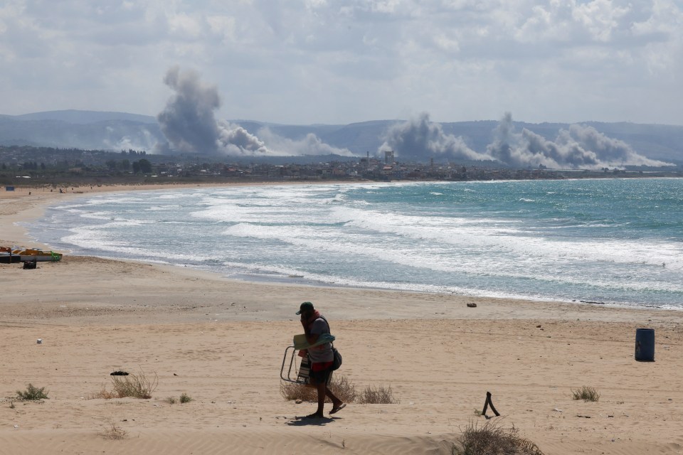 Un hombre camina por una playa mientras el humo se eleva sobre el sur del Líbano