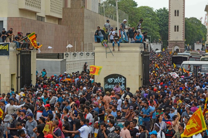 Una multitud de personas, algunas portando banderas nacionales y otras sentadas en postes de entrada.