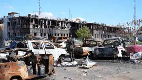 Un hombre vestido con uniforme de camuflaje y portando un arma camina entre vehículos incendiados en las calles de Omdurman.