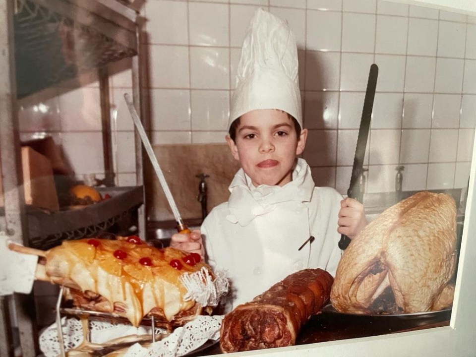 Simon de niño vestido con ropa blanca de chef y sosteniendo dos cuchillos.