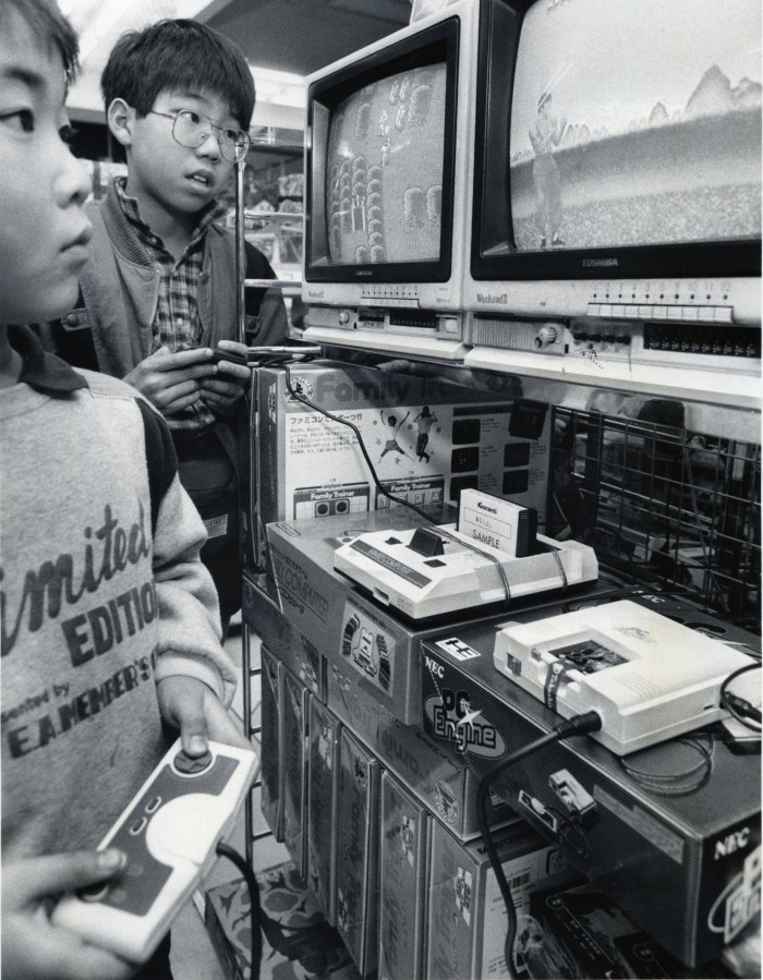 Dos niños se paran frente a una pantalla de televisión jugando un juego de computadora en una tienda. 