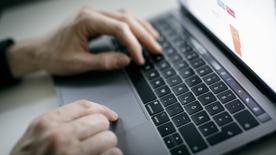 La mano de un hombre sobre el teclado de una computadora portátil.