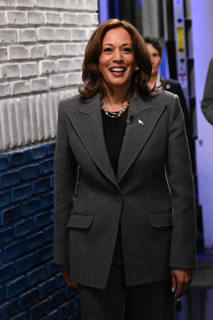 Una Kamala Harris sonriente en un área detrás del escenario. Lleva un traje gris sobre una blusa oscura.