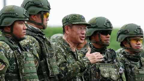 Wellington Koo habla entre varios soldados durante ejercicios de lanzamiento de misiles en Fangshan, condado de Pingtung, Taiwán. Los soldados visten uniformes de camuflaje y cascos, y algunos llevan gafas protectoras.