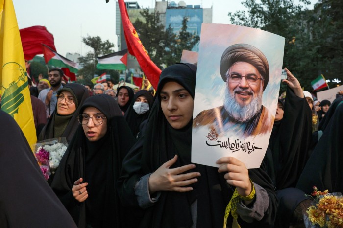 Los manifestantes en la Plaza Palestina de Teherán sostienen fotografías del líder de Hezbollah, Hassan Nasrallah, quien murió en un ataque aéreo israelí. Entre la multitud hay mujeres con hijabs negros, algunas portando banderas y flores.