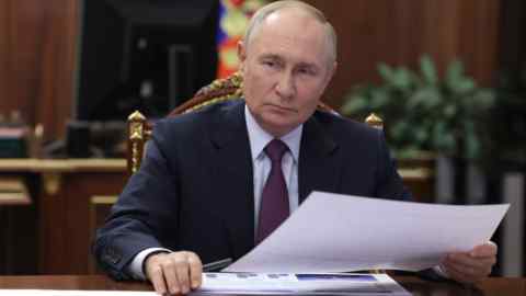 Vladimir Putin está sentado en un escritorio, sosteniendo un documento, durante una reunión en el Kremlin en Moscú.