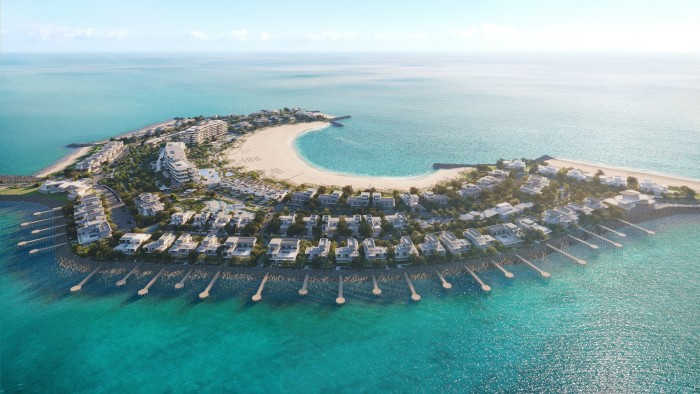 Una vista aérea de un lujoso resort isleño con una playa en forma de media luna rodeada de aguas turquesas. Cuenta con una combinación de villas frente al mar, estructuras sobre el agua y paisajes exuberantes.