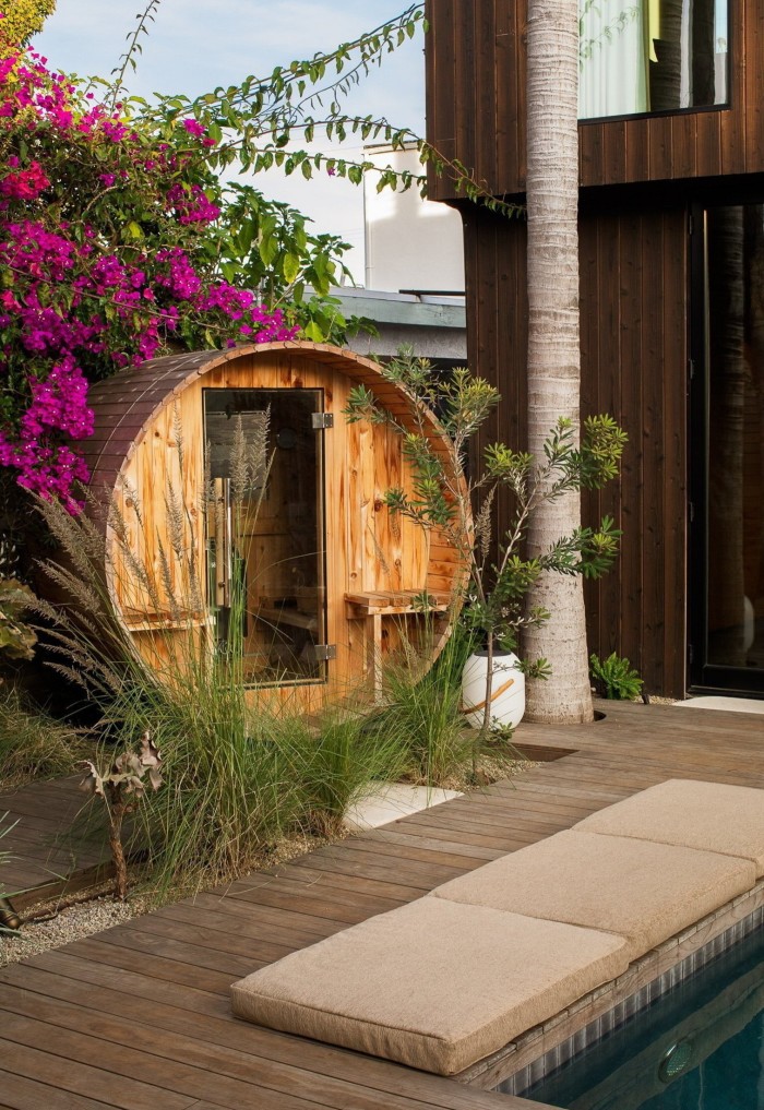 Una sauna de madera estilo barril ubicada en un exuberante jardín tropical