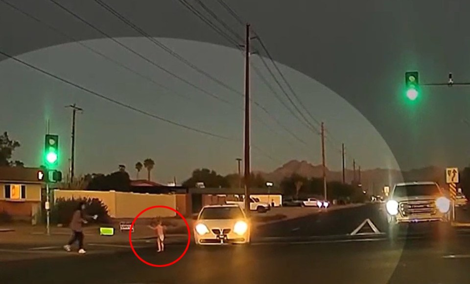 Una mujer cercana corre hacia la carretera para recogerlo justo cuando un auto se desvía para evitar atropellarlo.